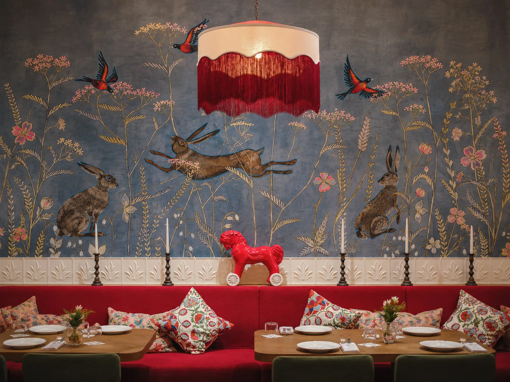 The dining room at Pechka, with hares and birds painted on the wall above a red banquette