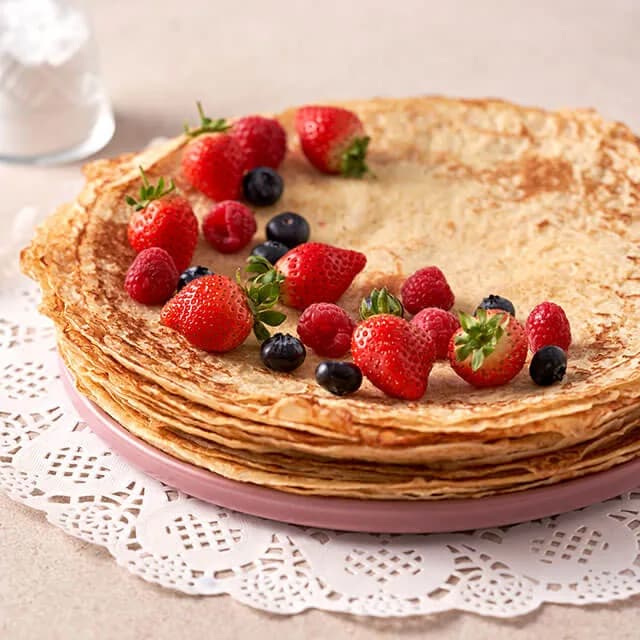 A stack of blini topped with strawberries, raspberries and blueberries