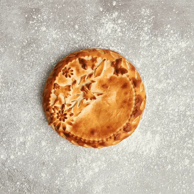 A Russian pie decorated with hand-cut pastry flowers, baked golden