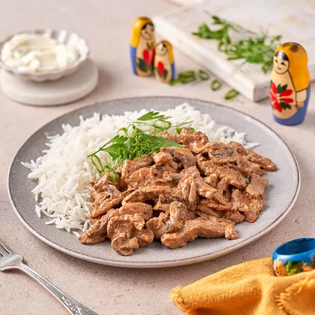 Beef stroganoff with rice and sour cream, matryoshka dolls behind the plate